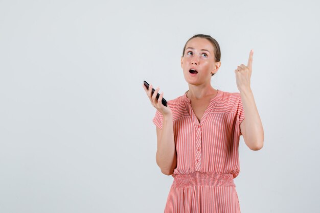 Giovane donna rivolta verso l'alto e tenendo il telefono cellulare in abito a righe vista frontale.