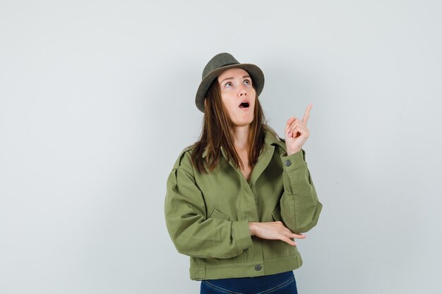 Giovane donna rivolta verso l'alto in giacca pantaloni cappello e guardando stupito