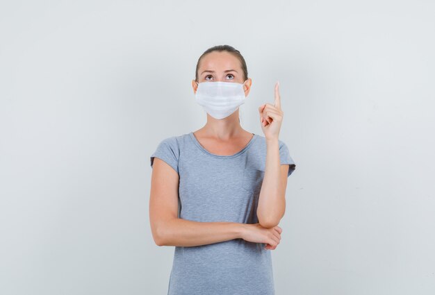 Giovane donna rivolta verso l'alto in maglietta grigia, maschera e sguardo concentrato, vista frontale.