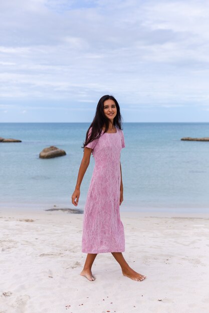 Giovane donna romantica con lunghi capelli scuri in un vestito sulla spiaggia sorridendo e ridendo divertendosi da solo