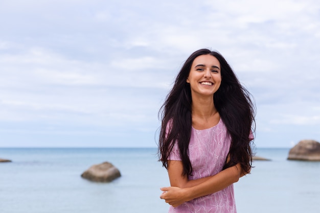 Giovane donna romantica con lunghi capelli scuri in un vestito sulla spiaggia sorridendo e ridendo divertendosi da solo