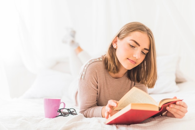Giovane donna sdraiata sul letto a leggere il libro