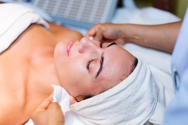 Giovane donna sdraiata sul tavolo del cosmetologo durante la procedura di ringiovanimento