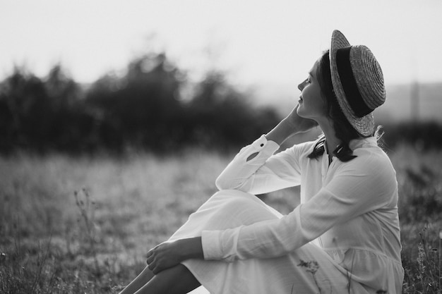 Giovane donna seduta in abito bianco e cappello a terra