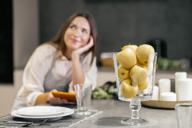 Giovane donna seduta in cucina e guardando pensierosa