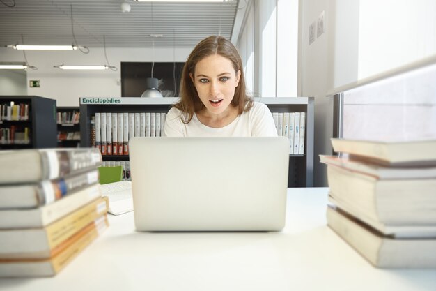 Giovane donna seduta in libreria con il computer portatile