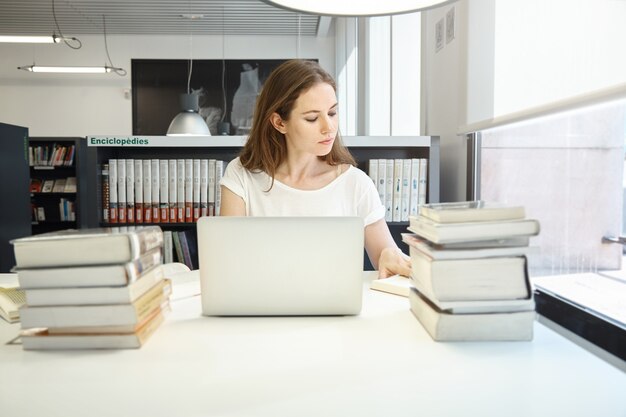 Giovane donna seduta in libreria con il computer portatile