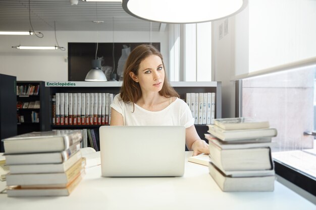 Giovane donna seduta in libreria con il computer portatile