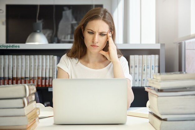 Giovane donna seduta in libreria con il computer portatile