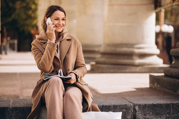 Giovane donna seduta sulle scale in città e leggere la rivista e parlare al telefono