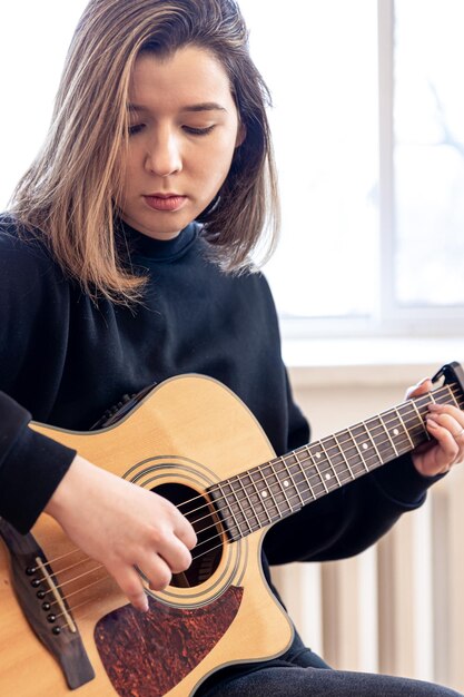 Giovane donna seria che suona la chitarra acustica a casa