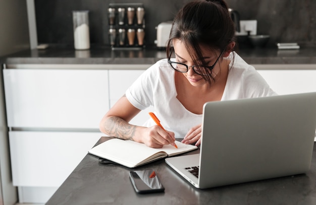 Giovane donna seria concentrata che usando le note di scrittura del computer portatile.