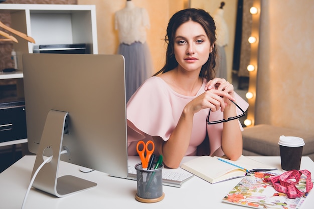 Giovane donna sexy alla moda in abito di lusso rosa, tendenza estiva, stile chic, stilista che lavora in ufficio sul computer