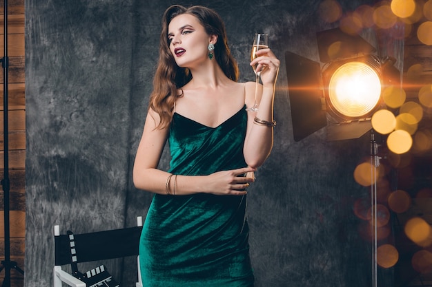Giovane donna sexy alla moda sul cinema dietro le quinte, festeggia con un bicchiere di champagne
