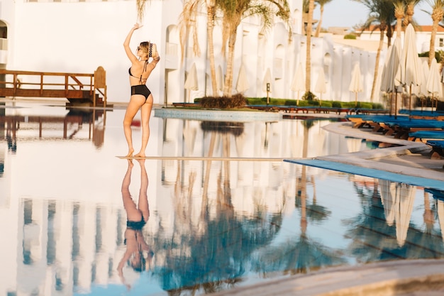 Giovane donna sexy, indossando il costume da bagno nero alla moda, bikini, vicino alla grande bella piscina, resort. Hotel. Felice ora legale, vacanze, vacanze, spa