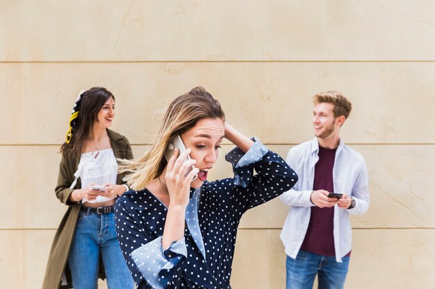 Giovane donna sorpresa che parla sul telefono cellulare che sta davanti agli amici che se lo esaminano