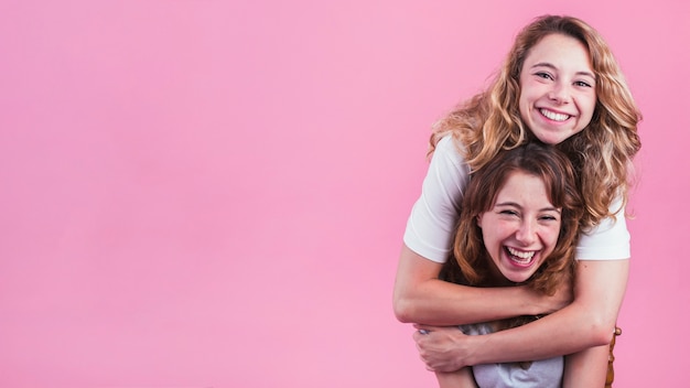 Giovane donna sorridente che abbraccia il suo amico da dietro contro fondo rosa