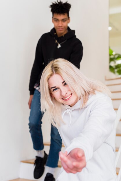 Giovane donna sorridente che cammina con il suo ragazzo che mostra mano verso la macchina fotografica