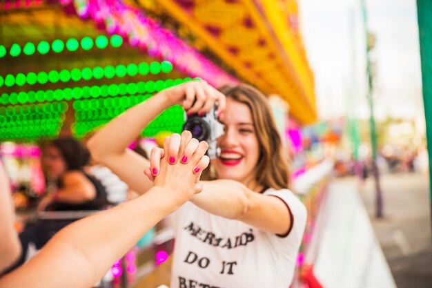 Giovane donna sorridente che cattura foto dalla mano della holding della macchina fotografica del suo amico