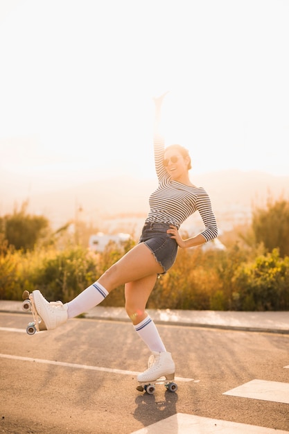 Giovane donna sorridente che equilibra sul pattino del rullo contro luce solare luminosa