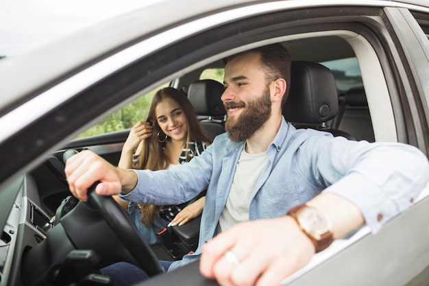 Giovane donna sorridente che esamina il suo ragazzo che conduce automobile