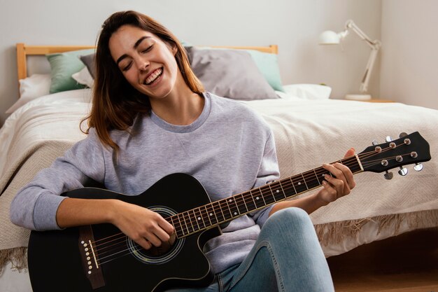 Giovane donna sorridente che gioca chitarra a casa