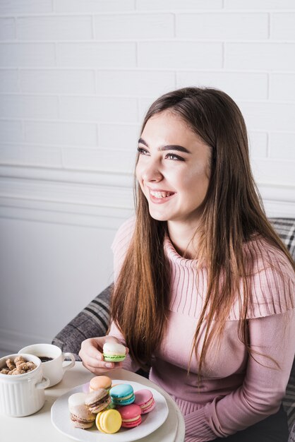 Giovane donna sorridente che gode mangiando i maccheroni variopinti in piatto bianco