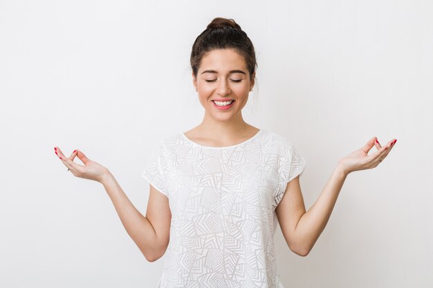 Giovane donna sorridente che medita, tenendo le mani nel gesto di yoga, sentendosi calma e positiva, occhi chiusi