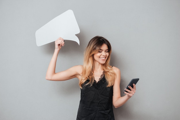 Giovane donna sorridente che per mezzo del telefono cellulare e tenendo fumetto