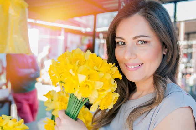 Giovane donna sorridente che seleziona fiori freschi. Primo piano profilo ritratto di una bella e giovane donna godendo e sentire l&#39;odore di un mazzo di fiori, mentre in piedi in una fresca stalla di mercato floreale durante una giornata di sole all&#39;aperto.
