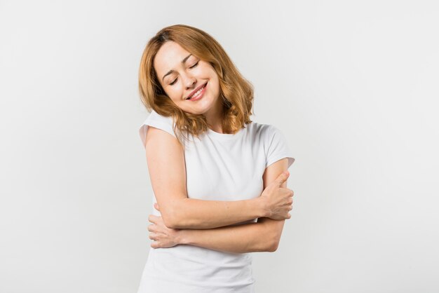 Giovane donna sorridente che si abbraccia contro il fondo bianco