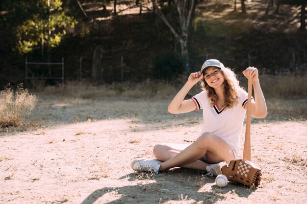 Giovane donna sorridente che si siede al campo di baseball