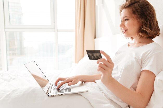 Giovane donna sorridente che si siede all'interno per mezzo del computer portatile