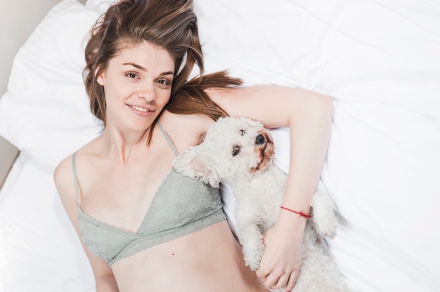 Giovane donna sorridente che si trova sul letto con il suo cane amichevole