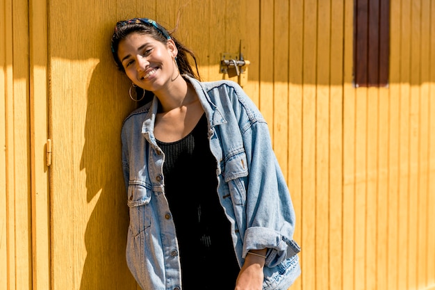 Giovane donna sorridente che sta contro la parete di legno