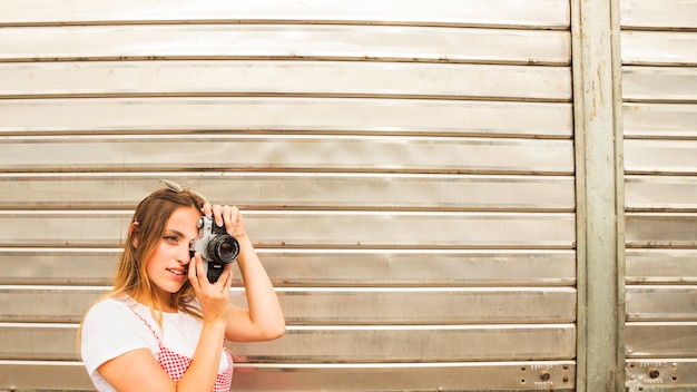 Giovane donna sorridente che sta davanti allo sportello che prende foto con la macchina fotografica