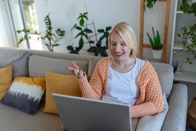 Giovane donna sorridente che usa il laptop a casa guardando lo schermo in chat con un tutor aziendale in videoconferenza che segue il concetto di ecoaching della formazione online della webcam