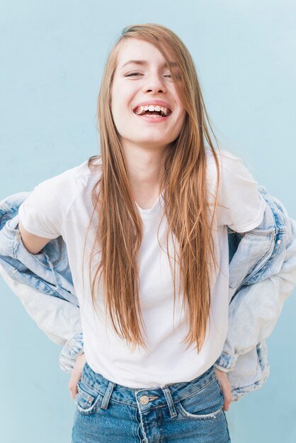 Giovane donna sorridente con capelli biondi lunghi che stanno sul contesto blu