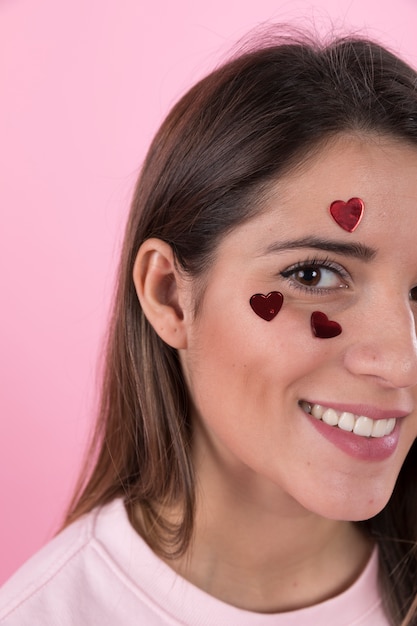 Giovane donna sorridente con cuori di ornamento sul viso