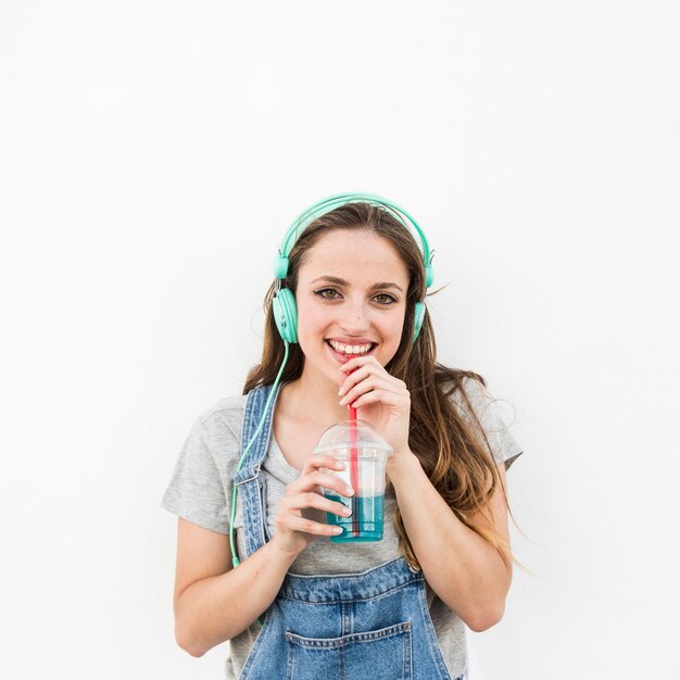 Giovane donna sorridente con la cuffia sulla sua testa che beve succo