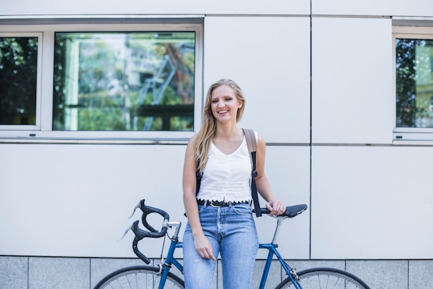 Giovane donna sorridente con la sua bicicletta che sta all&#39;aperto