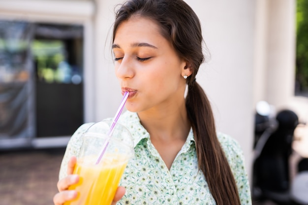 Giovane donna sorridente e bere un cocktail con ghiaccio in un bicchiere di plastica con paglia