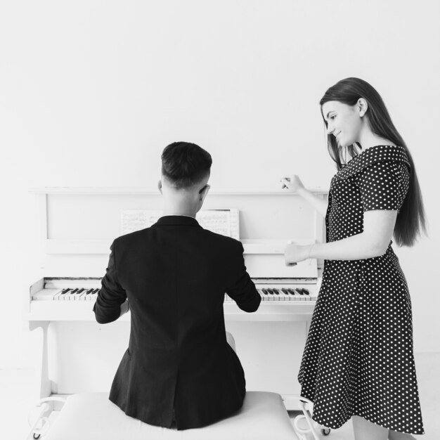 Giovane donna sorridente graziosa che esamina uomo che gioca piano