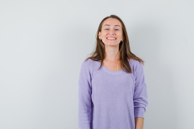 Giovane donna sorridente in camicetta lilla e guardando allegra