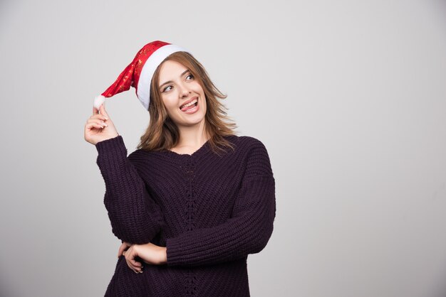 Giovane donna sorridente in cappello di Babbo Natale in piedi e in posa.