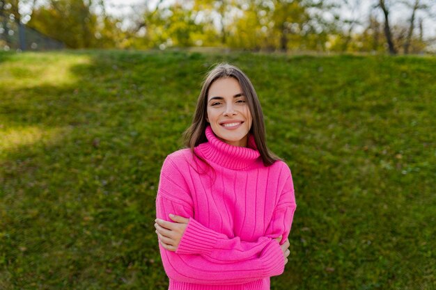 Giovane donna sorridente in maglione rosa che cammina nel parco verde