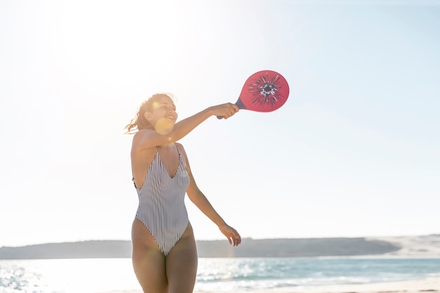 Giovane donna sorridente sulla spiaggia che gioca a tennis