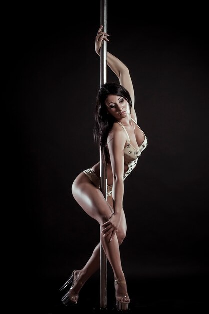 Giovane donna sottile pole dance su uno sfondo nero studio