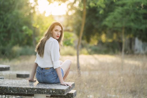 Giovane donna spagnola attraente che indossa pantaloncini con una camicia bianca in un parco in una giornata di sole