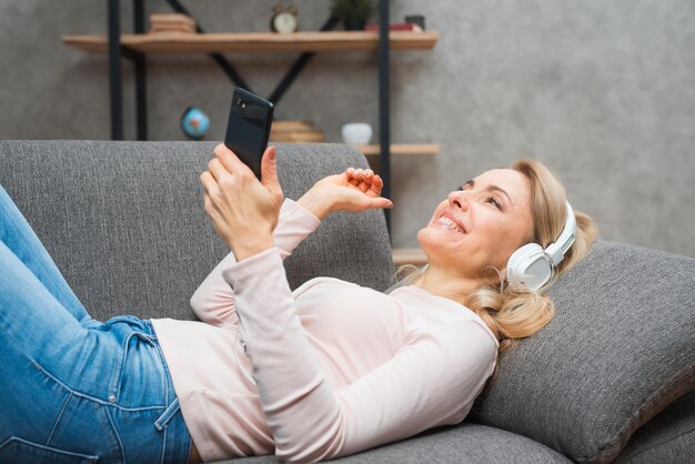 Giovane donna spensierata che gode della musica sul cellulare della tenuta della cuffia a disposizione